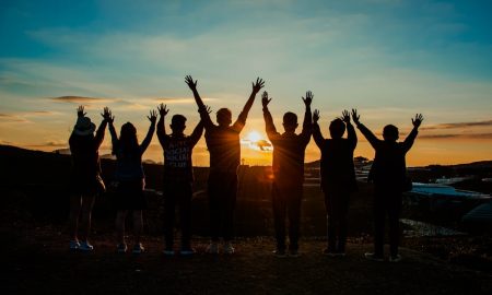 Weekly Horoscope - A team raising hands during sunset.